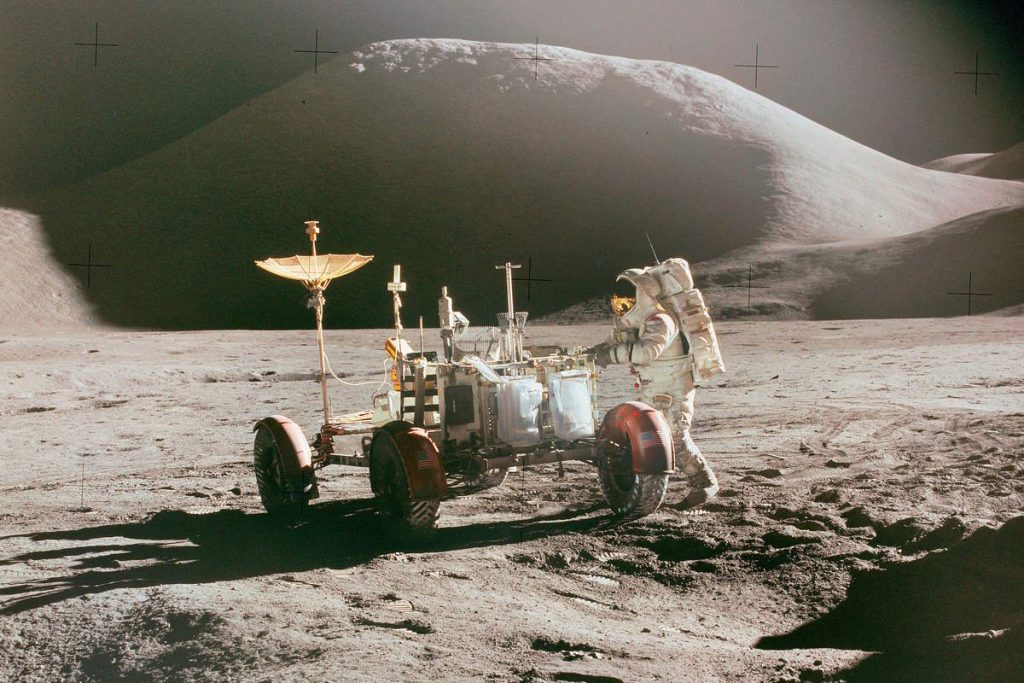 Apollo 15 astronaut Jim Irwin stands at the Lunar Rover, with Mons Hadley as a backdrop